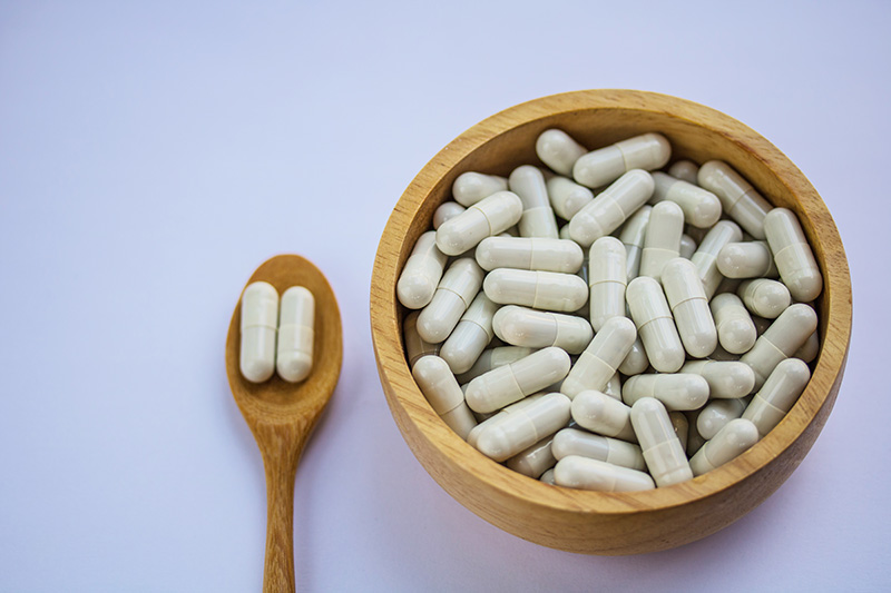 Capsule pills in wooden spoon and wooden bowl on white background.